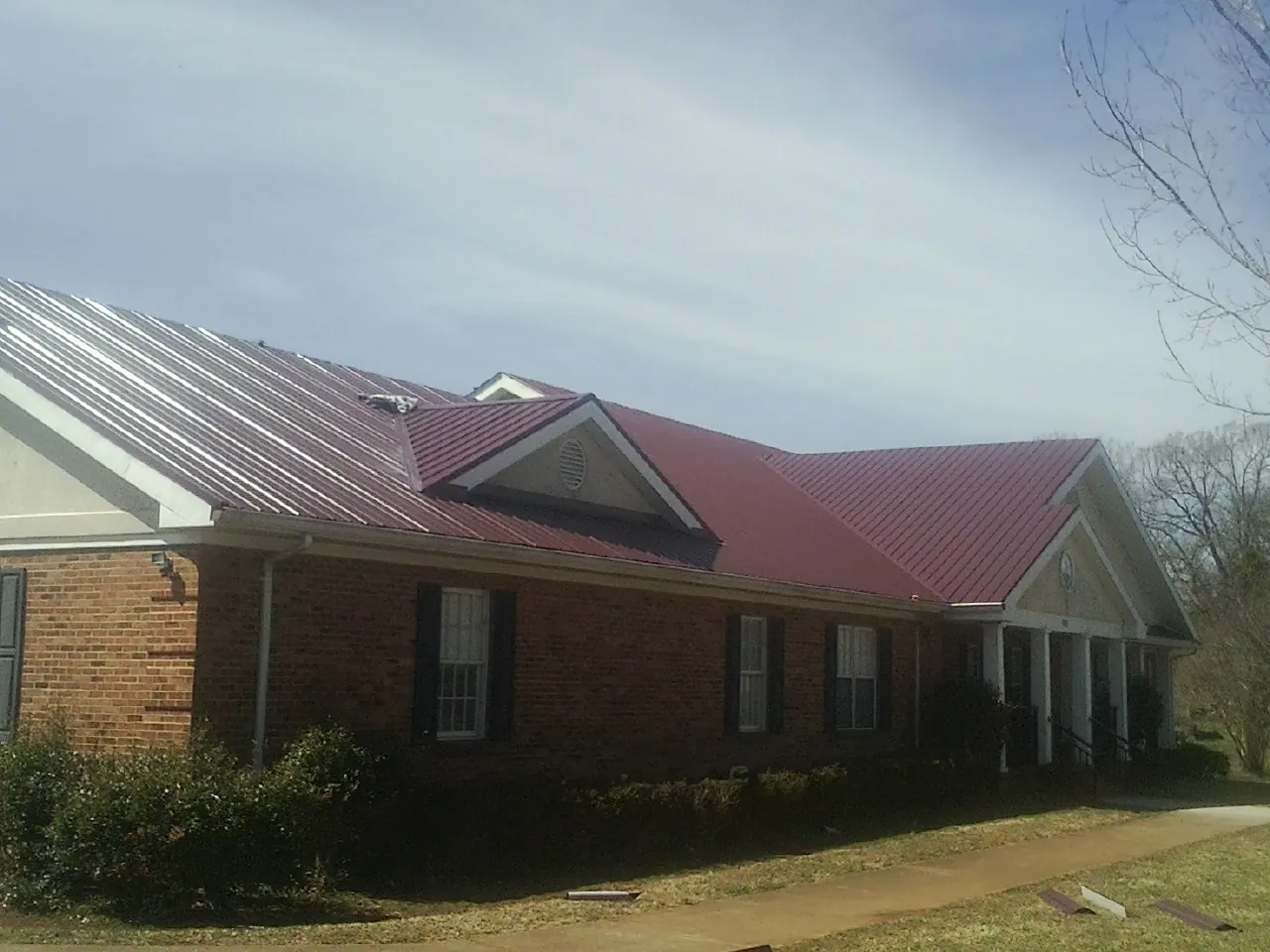 Red metal roof with gabled entries on a long brick building, from a Hail Damage Roof Repair job in Philadelphia