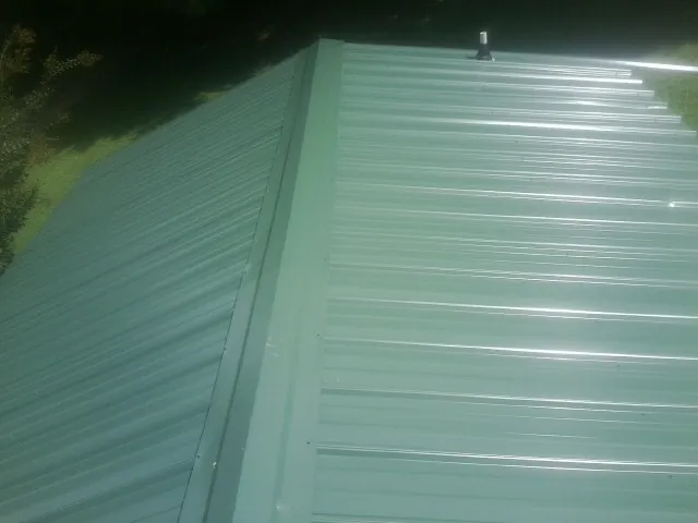 New green metal panels meeting at the ridge of a roof — Flat Roof Repair work by our crew in Philadelphia