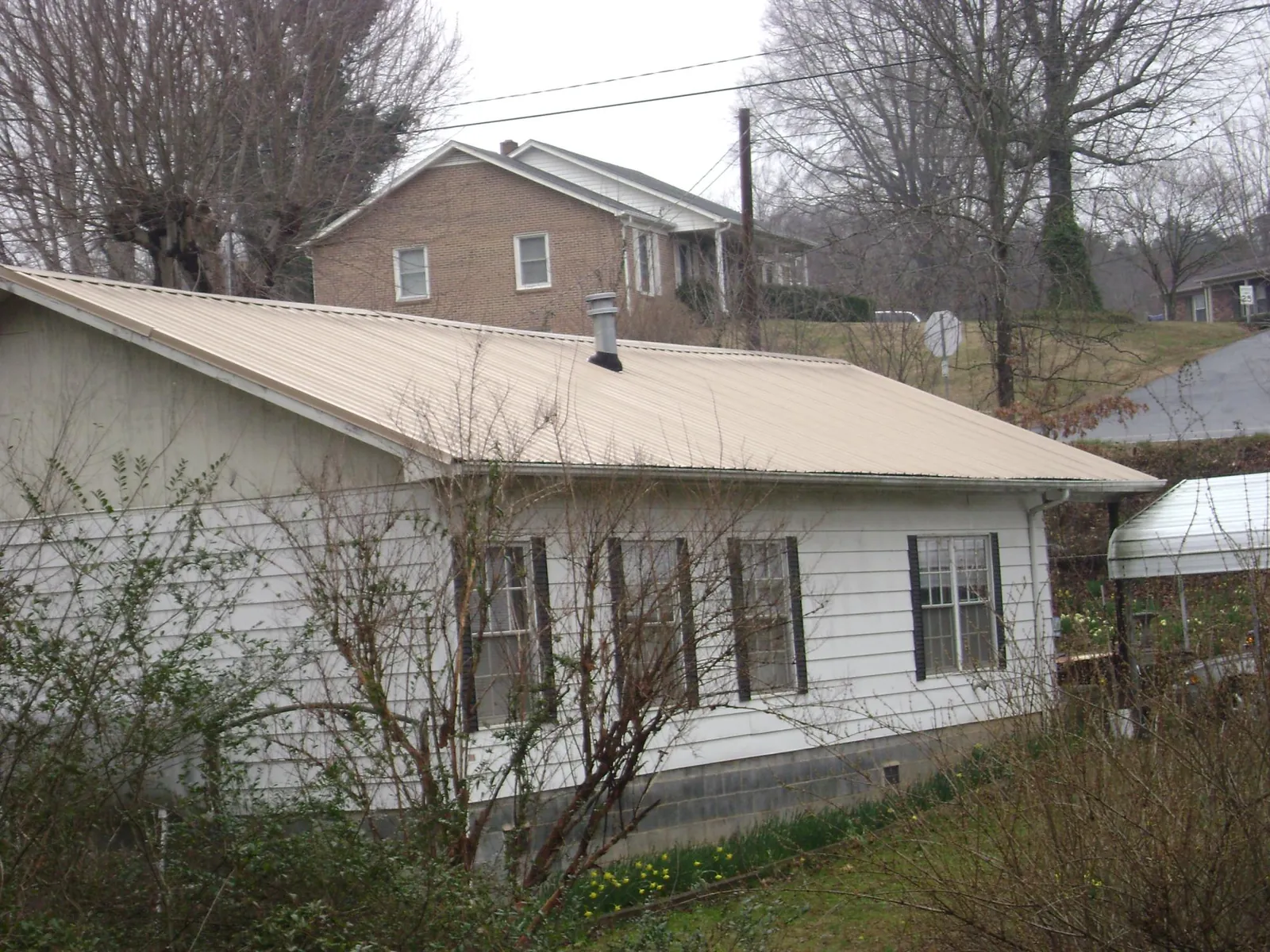 Tan metal roof on a white sided house set into a hillside — Commercial Roofing by Roofing Brothers in Philadelphia